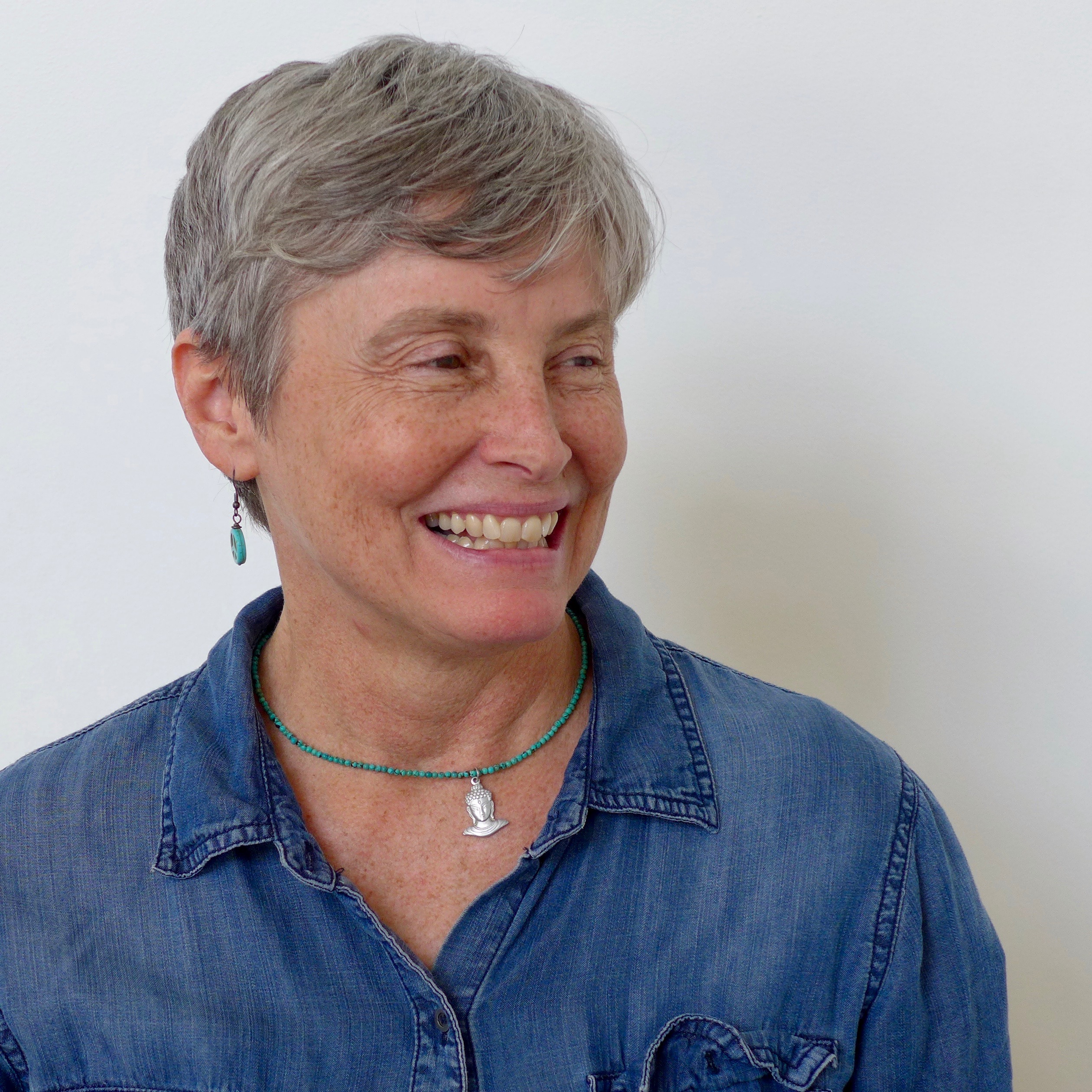Smiling woman wearing a blue shirt and buddha necklace